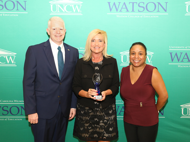 Alumni Award recipient smiles with two others at ceremony