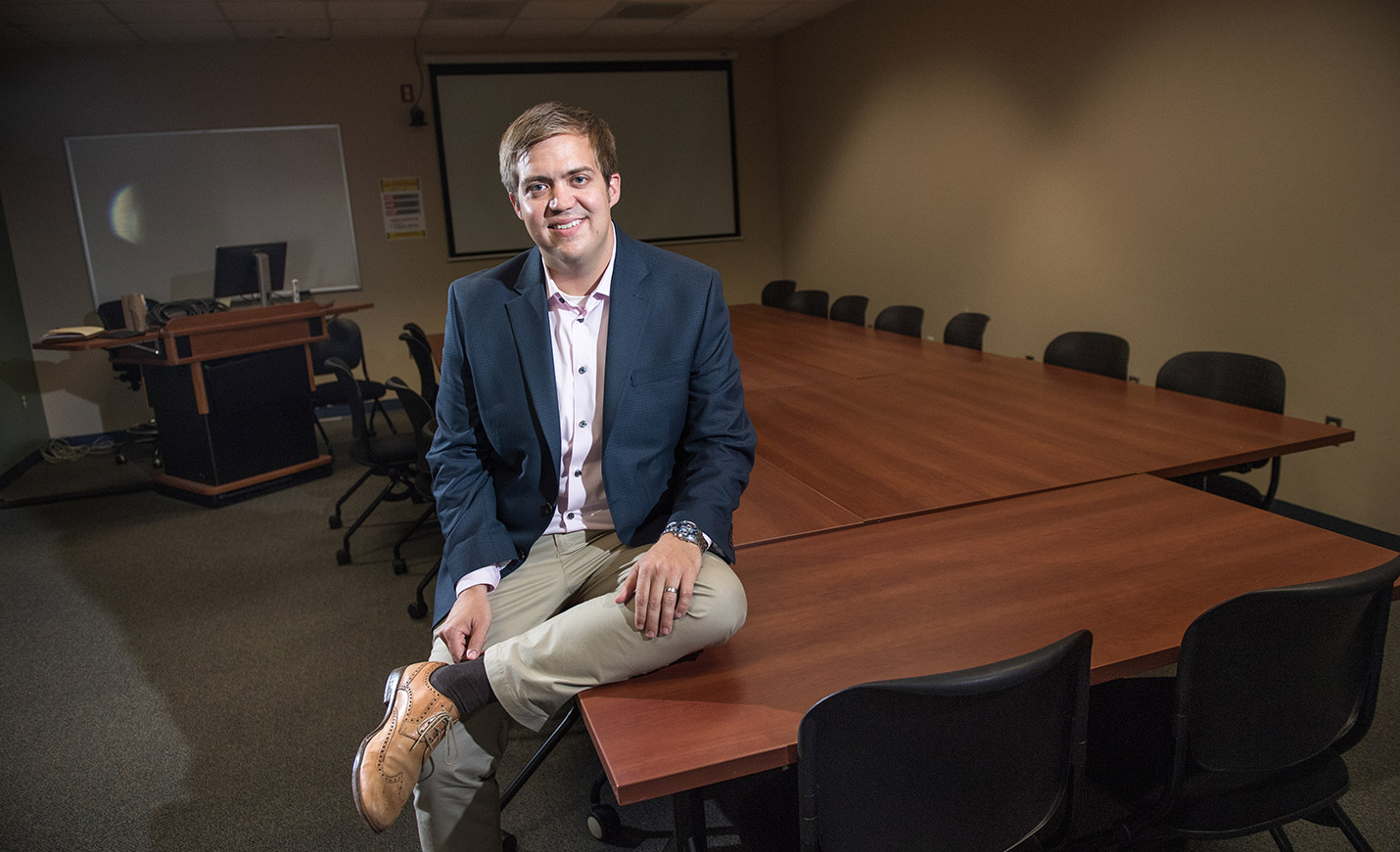 UNCW Associate Professor Aaron King sitting on a table in a classroom