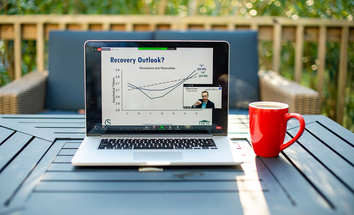 An open laptop on an outdoor table with a chart showing business trends; a coffee cup sits next to it