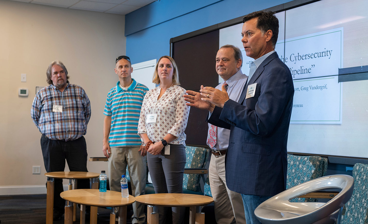 A speaker standing next to other presenters talks during a conference on cybersecurity